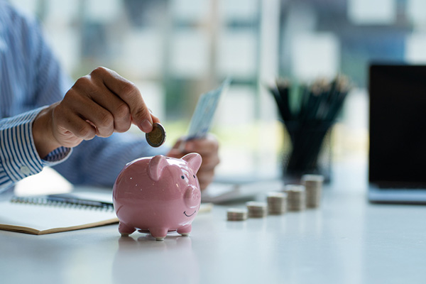 Hand of businessman putting coins into piggy bank